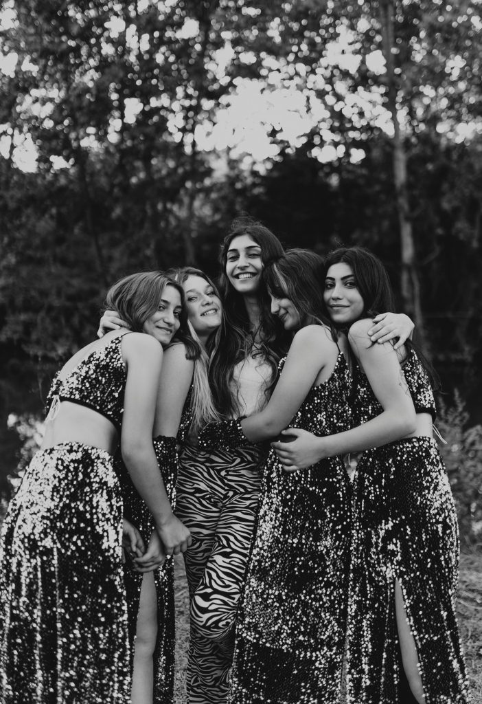Five young women hugging each other in a forest.