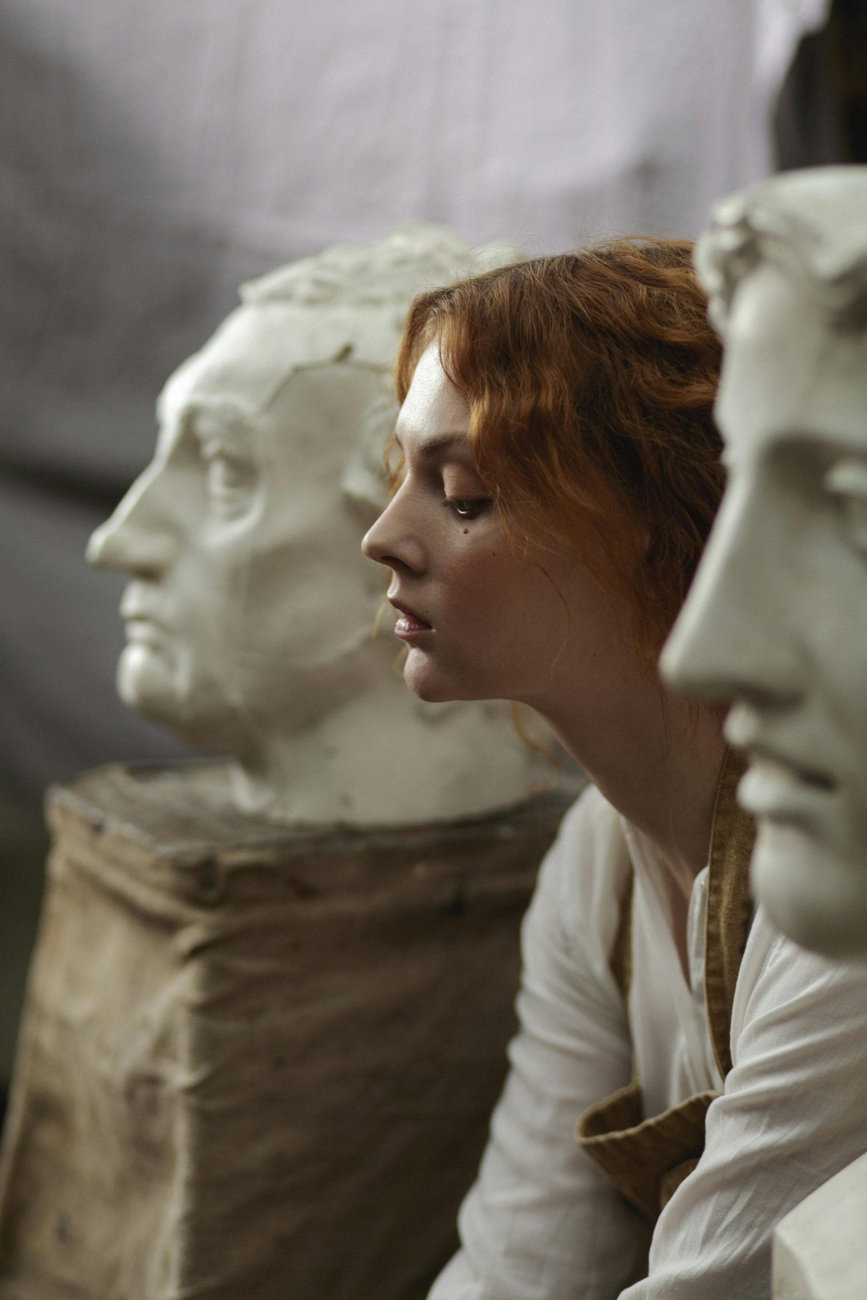 Redhead woman sitting between two Ancient Greek statues,